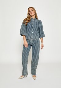 Jeansowy zestaw z wzorzystą, jasnoniebieską, krótką kurtką z bufkami i dopasowanymi spodniami o prostych nogawkach, połączony z beżowymi szpilkami w szpic.