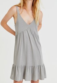 Vestido gris sin mangas con escote en V, cintura fruncida y dobladillo con volantes. Tejido suave con una textura lisa y un diseño casual.