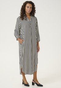 Striped long dress in cream and black, featuring a collar, button placket, and side pockets. The fabric is lightweight with a smooth texture.