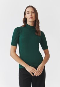 Zelený krátký rukáv top s obojkovým výstřihem, vyrobený z texturovaného materiálu. Tvarující design zvýrazňuje siluetu. Jednoduchý a elegantní.