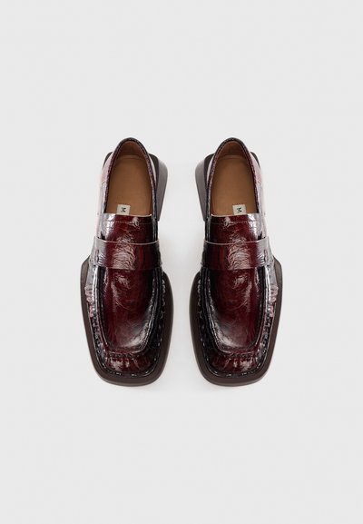 Pair of glossy dark red leather loafers with square toes and black sole, viewed from above on a white background.