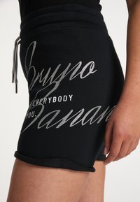 Svarta bomullsshorts med silverglittrig text. Designen inkluderar en dragsko i midjan och uppvikta fållar.