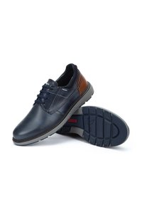 Zapatos de cuero navy con acentos marrones, diseño con cordones, suela de goma y suela gris contrastante. Textura suave y forma moderna.