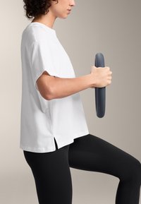 Vit bomullströja med korta ärmar och sidofickor, tillsammans med svarta tights. Personen håller ett grått, runt träningsredskap.