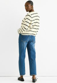 Cream striped sweater with black lines, soft texture, paired with mid-blue straight-leg jeans and black flats, viewed from the back.