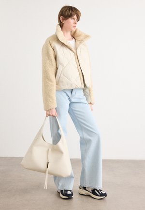 Quilted beige jas met zachte, pluizige crèmekleurige mouwen; gecombineerd met lichtblauwe jeans en een grote off-white tas met een ritsdetail.