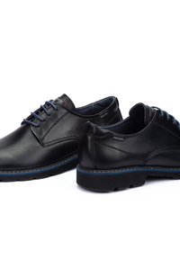 Zapatos de cuero negro con un acabado suave, puntera redonda, acentos azules en la suela y los cordones, y detalles de costura sutiles. Logo de la marca visible.