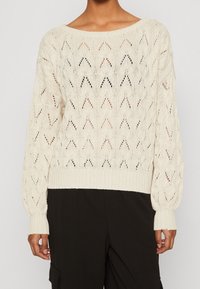 Krämfärgad, stickad tröja med en löst sittande passform, har ett zigzag-mönster, bred båtutskärning och ribbade manschetter och nederkant.