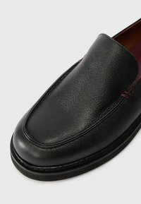 Μαύρο δερμάτινο παπούτσι slip-on με υφή, στρογγυλή μύτη και ελάχιστες ραφές αντίθετης απόχρωσης στο επάνω μέρος.