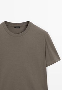 T-shirt taupe à manches courtes avec col rond côtelé, tissu lisse et bord de manche cousu, présenté à plat sur fond blanc.