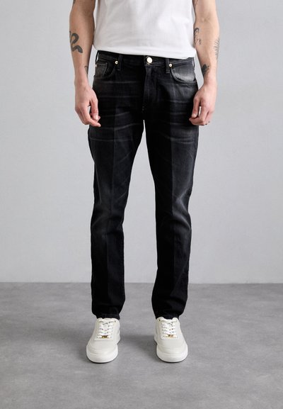 Černé džíny z denimu s úzkým střihem, s jemným vyšisováním, zlatým kováním a klasickým pětipocket designem, spárované s bílými teniskami.