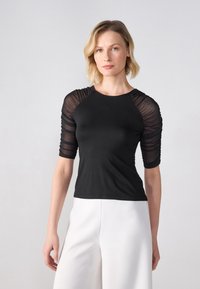 Top negru cu mâneci scurte, eficiente și transparente, și un corset ajustat. Decolteul este rotund, iar textura este netedă și elegantă.