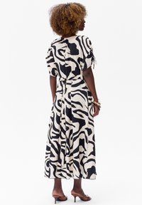 Maxi jurk in crème met zwarte gedurfde zebrapatronen, met korte mouwen, een strik taille en een vloeiende silhouet.