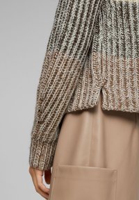 Maglione a maglia grossa in tonalità beige e marrone con righe verticali a coste. Presenta un orlo diviso ed è abbinato a una gonna di pelle beige liscia.