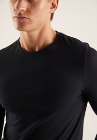 Črna majica z dolgimi rokavi iz gladkega blaga. Ima klasičen okrogel izrez in običajen kroj, prikazuje subtilno teksturo brez vzorcev.