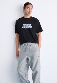 Schwarzes Baumwoll-T-Shirt mit Grafikdruck, kombiniert mit grauen Sweatpants mit Kordelzug und gesticktem Logo am Bein.