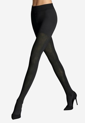 Beine mit schwarzen gemusterten Strumpfhosen und schwarzen High Heels, die sich vor einem einfachen hellen Hintergrund kreuzen.