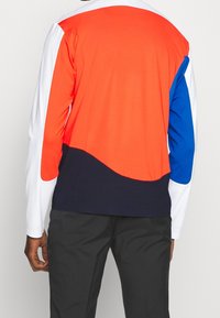 Långärmad skjorta med paneler av orange, blått, vitt och marinblått. Mjuk tyg med en slät textur och böljande färövergångar.