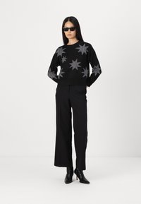 Black knitted sweater with silver star patterns, paired with high-waisted black wide-leg pants and black ankle boots.
