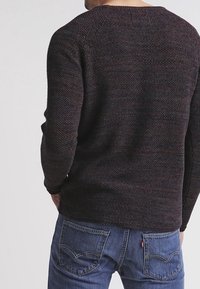 Maglione lavorato a maglia in colori scuri, con un motivo testurizzato e un ampio scollo a giro. Abbinato a jeans in denim blu.