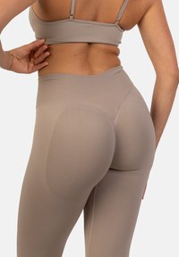 Bežové rebrované legíny s vysokým pásom a bezšvovým dizajnom, ktoré sa zužujú pri členku a majú akcentovanú zadnú časť.