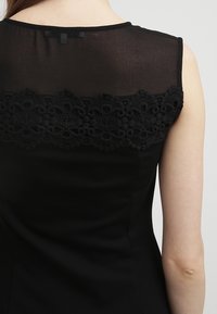 Mustapuku, jossa on läpinäkyvä musta takapaneeli, jossa on monimutkaista pitsikoristelua, rakenteellinen muoto ja hihaton design.