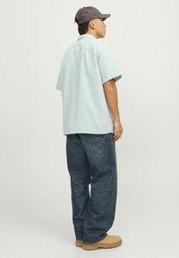 Chemise à manches courtes, à carreaux bleu clair, coupe décontractée, associée à un jean baggy bleu et des bottes de travail marron, avec une casquette grise.