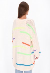 Przesadny sweter dzianinowy w kolorze kremowym z kolorowymi, nieregularnymi paskami w zielonym, pomarańczowym, purpurowym i niebieskim. Luźny krój i teksturowany wzór.
