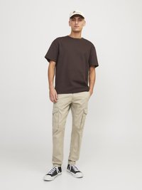 Tricou scurt, din bumbac, maro, purtat cu pantaloni cargo ușor bej, care au buzunare laterale. Adidași negri și albi completează ținuta.