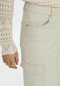 Helles beiges Cargo-Rock aus Baumwolle mit Seitentaschen, gesteppten Details und glatter Textur, kombiniert mit einem gestrickten cremefarbenen Pullover.