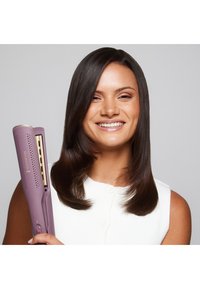 En lyserød og gylden hårglatter holdt i den ene hånd. Den har en tekstureret krop, flade plader og et fremtrædende brandlogo med ventilationshuller.