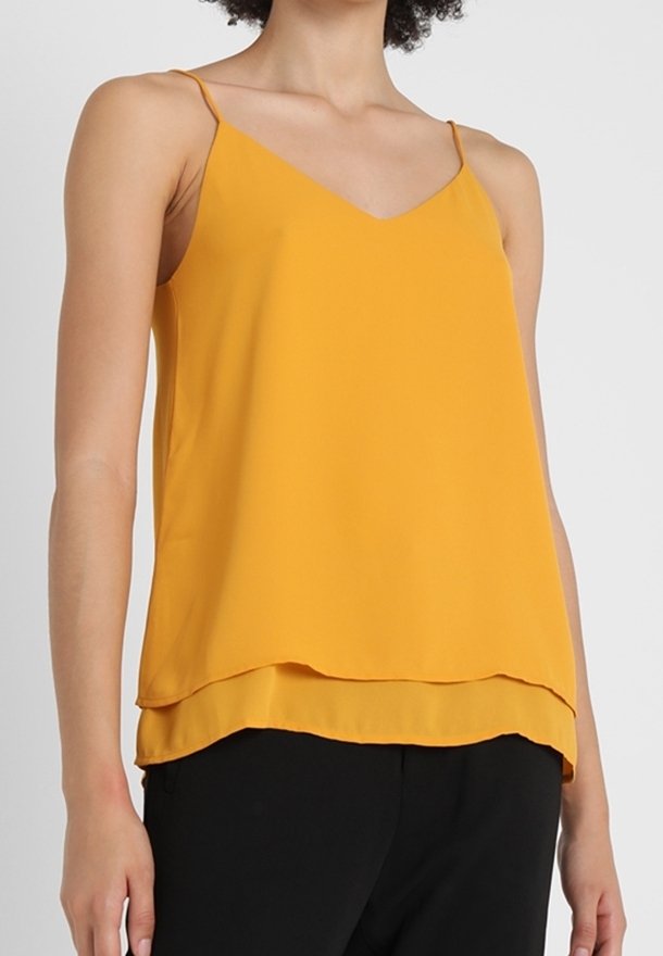 Haut camisole jaune sans manches à double couche avec fines bretelles porté avec un pantalon noir sur une personne.