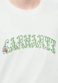 Άσπρο βαμβακερό μπλουζάκι με πράσινο pixel κείμενο και λουλουδένιο σχέδιο. Το κείμενο σχηματίζει τόξο μπροστά, με ροζ τριαντάφυλλο στην αριστερή πλευρά.