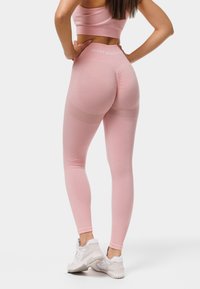 Leggings roses et crop top assorti en matériau élastique doux, dotés d'un design texturé et d'un logo sur la ceinture, associés à des baskets blanches.