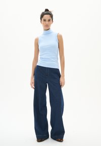 Un haut sans manches à col roulé bleu clair associé à un pantalon en denim bleu foncé à jambes larges. Des chaussures plates à imprimé léopard noir et marron complètent l'ensemble.