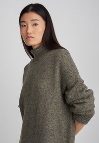 Olive rohelise värvi kudumisega sviiter, millel on kõrge kaelus, üleriigiline lõige ja tekstureeritud kude. Omab soonikestega mansette ja pehmeid, mugavaid jooni.