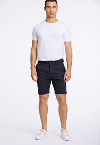Marinblå shorts i bomullsblandat tyg med uppvikt fåll, matchade med en vit t-shirt med rund hals och vita sneakers.