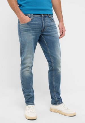Slim-fit blue jeans made of denim, featuring a faded wash, front pockets, and stitched detailing. Paired with white sneakers.