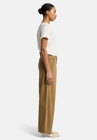 T-shirt beige chiaro con maniche arrotolate, abbinato a pantaloni larghi a vita alta di colore beige chiaro e scarpe con tacco a punta beige. Diverse texture sottili.