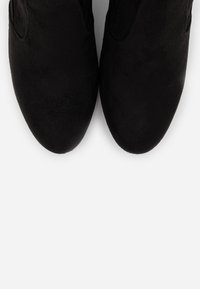 Un par de zapatos de ante negro con punteras redondeadas sobre un fondo gris claro, vistos desde arriba.