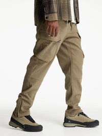 Cargo byxor i ljusbeige tyg, med flera fickor, en slim fit-design och dragkedjeförsedda anklar. I kombination med svarta och beige skor.