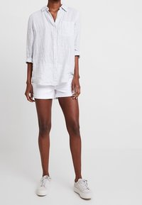 Ljusgrå, randig skjorta med lång ärm som är uppvikt till armbågarna, matchad med vita shorts och vita sneakers. Har en bröstficka.