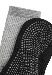 Paire de chaussettes avec une chaussette grise côtelée et une chaussette noire présentant des points en caoutchouc antidérapants sous la semelle.