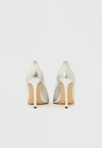 Sølvfarvede højhælede sko med en metallisk tekstur, spids tå og en slank stilet hæl. Har et lille logo på bagsiden.