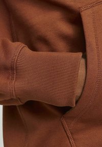 Brun sweatshirt med ribbede manchetter, blød tekstur og synlige sømme. Den hættebærende design har en forlommekasse for funktionalitet.