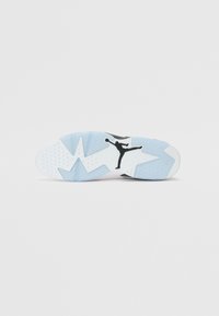 Fehér sportcipő talp, fekete Jumpman logóval, textúrált kék részletekkel és sokszínű mintázatú futófelülettel a tapadás érdekében.