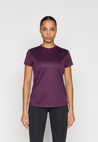 Lühikeste varrukatega lilla sportlik T-särk ümarate kaelusega. Riie tundub sile ja kergelt läikiv, koos mustade retuusidega.