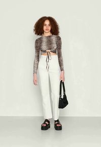 Top cropped de mangas longas às riscas brancas e pretas, calças brancas de cintura alta, sandálias pretas de plataforma e uma pequena mala preta de ombro.