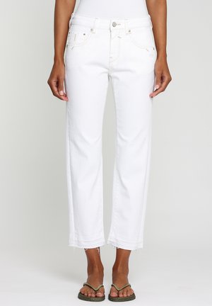 Jean blanc taille haute à jambes droites avec ourlet brut, porté par une personne aux pieds nus à la peau foncée sur un fond clair uni.