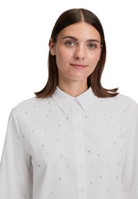 Witte button-up shirt met een kraag, versierd met verspreide zilveren en heldere versieringen over de voorkant.